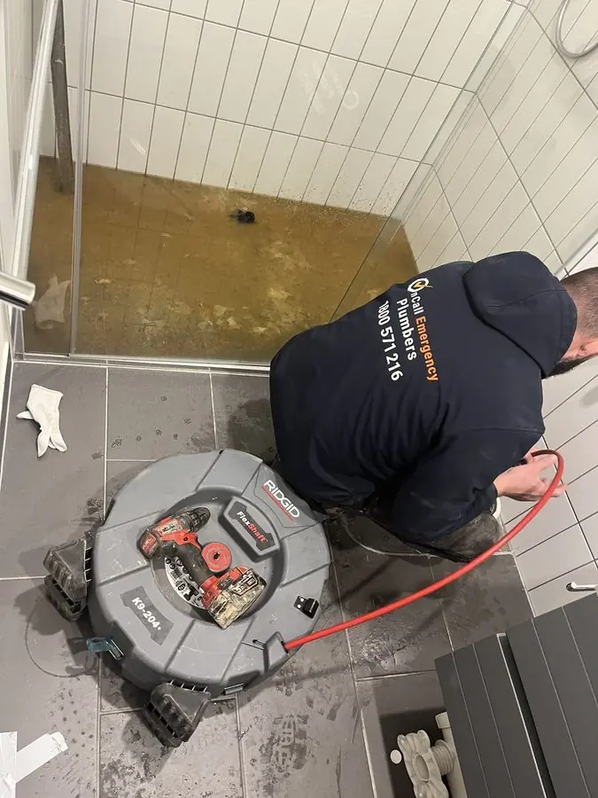 Plumber clearing a bathroom floor drain, Braeside