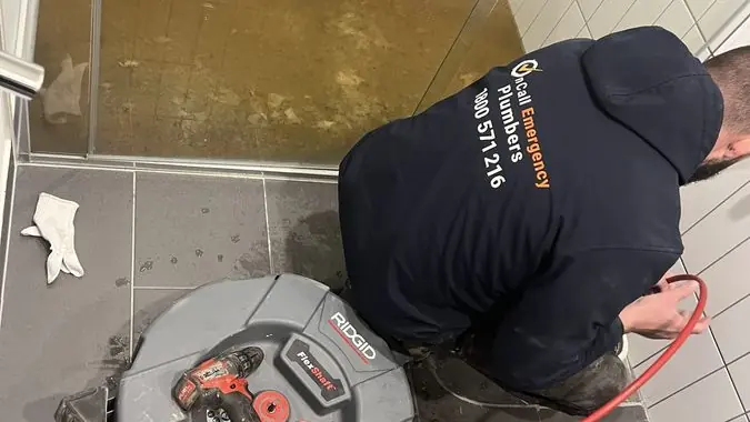 Plumber clearing a bathroom floor drain, Braeside